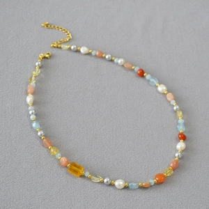 Dettaglio di collana con perle barocche, pietre colorate blu e una gemma gialla centrale