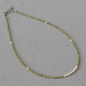 Detail of beaded necklace with green faceted stones and elegant white pearls