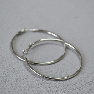 Close-up of oversized polished silver hoop earrings with pin closure on textured fabric