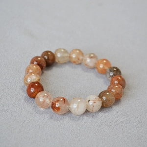 Macro detail of 10mm red rutilated quartz beaded bracelet on grey textured fabric