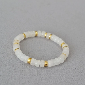 Macro shot of minimalist white beads and gold-plated spacers on a grey fabric background