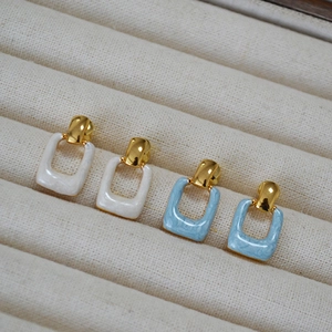 Detailed close-up of gold-plated square marble earrings on a beige velvet jewelry display