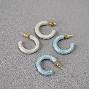 Close-up of cream and blue C-shaped enamel earrings with marble texture on fabric