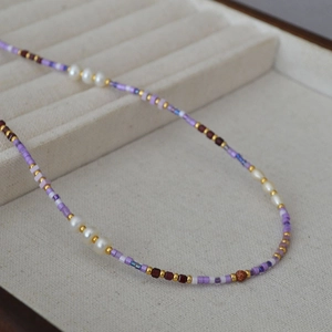 Close-up of violet beaded necklace with freshwater pearls and gold beads in a box