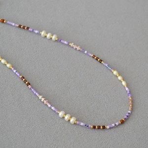 Elegant lavender seed bead necklace with white pearls and gold accents on textured grey fabric