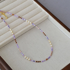 Close-up of handmade violet seed bead necklace with white freshwater pearls on beige tray
