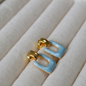 Macro view of geometric square stud earrings with light blue marble texture and gold plating