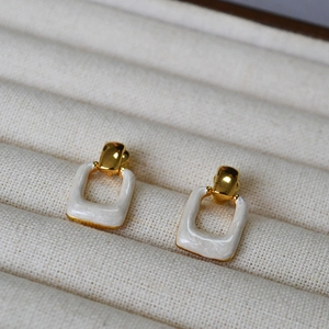 Macro detail of geometric square earrings with gold brass and white enamel finish