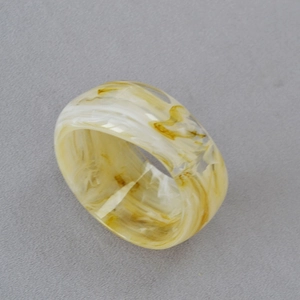 Gros plan d'une large bague en acrylique avec texture marbrée ambre et crème sur tissu gris