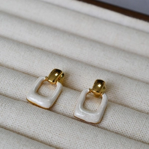 Detail of square enamel brass gold-plated earrings resting on white textured fabric