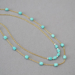 Detail of double-layer gold beaded chain with faceted turquoise stones on gray fabric