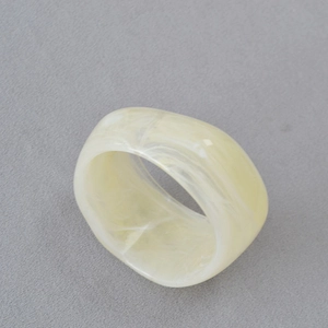 Vue macro d'une bague large en résine à texture marbrée crème sur fond en tissu gris