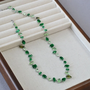 Elegant silver necklace featuring multi-shaped green gemstones on a cream velvet tray