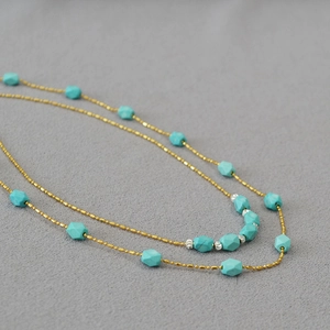 Macro detail of gold bead chain necklace featuring geometric turquoise stone accents