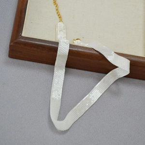 Close-up of handmade white beaded choker with diamond texture and gold lobster clasp