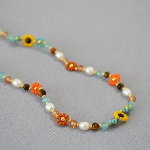 Détail de collier bohème avec fleurs tournesol tissées et perles baroques
