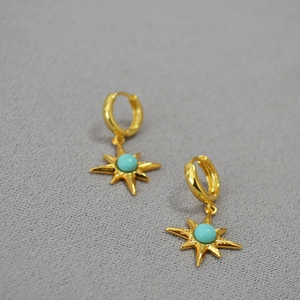 Detailed close-up of gold-plated starburst earrings with turquoise stone on grey fabric