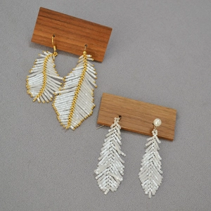 Detailed macro view of handmade white feather beaded earrings with golden accents