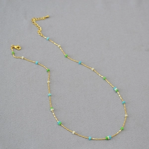 Detailed view of gold plated brass chain with colorful square beads on grey fabric