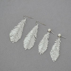 White hand-woven feather beaded earrings with pearls and hooks on grey fabric background