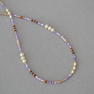 Close-up of violet glass seed beads and white freshwater pearls on a summer necklace