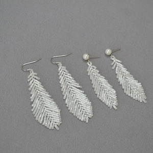 Macro shot of white handmade seed bead woven feather earrings on grey fabric