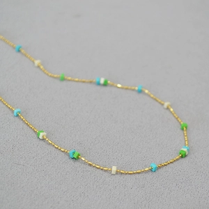 Close-up of gold-plated thin chain necklace with turquoise and white square stone beads