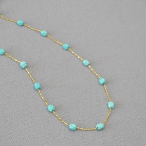 Detailed close-up of a gold bead chain necklace with faceted turquoise stone accents
