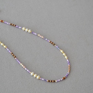 Macro detail of violet seed bead necklace with natural freshwater pearls on grey linen fabric