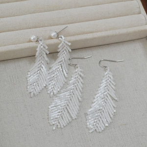 Close-up of handmade white beaded leaf earrings with pearl studs and metal hooks