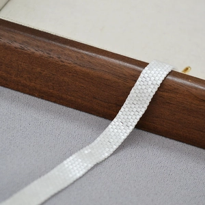Elegant white beaded ribbon necklace with handcrafted woven texture on a wooden box