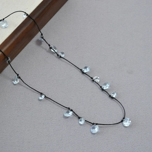 Dettaglio della collana minimalista in cordino nero con ciondoli in cristallo azzurro brillante