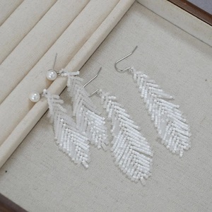 Detail of handmade white bead earrings in feather shape on a jewelry display tray