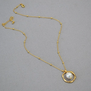 Macro shot of irregular golden ring pendant with a lustrous pearl on a beaded necklace