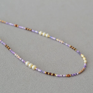 Detailed macro of handmade purple and gold seed bead necklace with white pearl accents