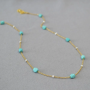 Detail of turquoise beads with textured silver spheres on a gold bead chain necklace