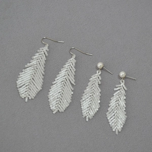 Macro detail of handmade white seed bead feather earrings with pearl accents on grey fabric