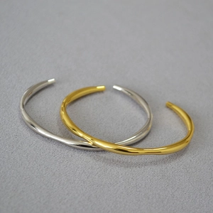 Detail of minimalist gold and silver open bangles with irregular fluid wave patterns