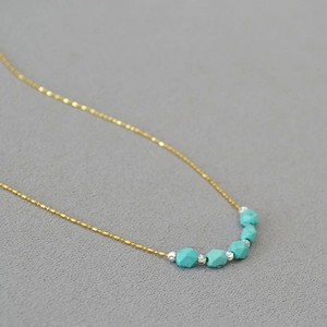 Detail of minimalist gold bead chain with faceted turquoise beads on a grey background