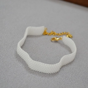 Macro detail of white hand-woven beaded choker featuring elegant wave pattern and gold clasp