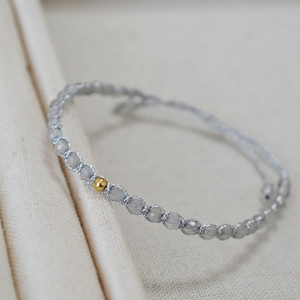 Détail macro d'un bracelet tissé main avec perles grises facettées et perle dorée