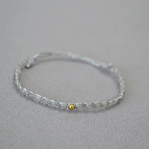 Gros plan d'un bracelet bohème avec de fines perles grises facettées et une bille dorée