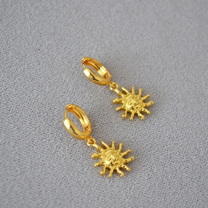Macro shot of minimalist gold plated sun charm hoop earrings on grey textured fabric