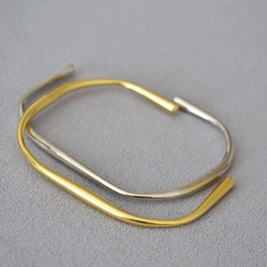 Detail von unregelmäßigen minimalistischen Gold- und Silberarmreifen auf Stoff