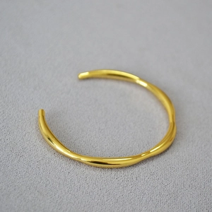 Macro detail of minimalist gold-plated bangle with irregular wavy organic line design