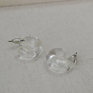 Macro shot of minimalist clear resin C-shaped earrings with silver pins on beige fabric