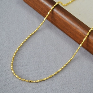 Minimalist brass gold plated rice bead necklace displayed on a luxury textured tray
