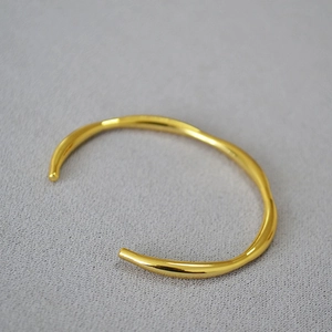 Macro shot of minimalist gold plated cuff bangle with irregular organic wavy lines