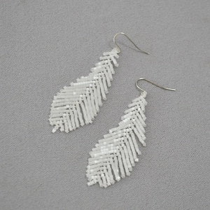 Detailed view of hand-woven white bead earrings in feather shape on textured fabric