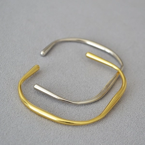 Detailaufnahme von goldenen und silbernen geometrischen Armreifen auf grauem Stoff